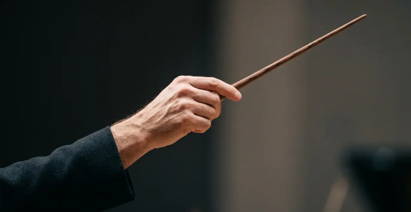 A conductor's hand holding a baton frozen mid-gesture against a minimalist background, capturing the decisive moment of non-verbal communication in orchestral leadership