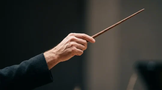 A conductor's hand holding a baton frozen mid-gesture against a minimalist background, capturing the decisive moment of non-verbal communication in orchestral leadership
