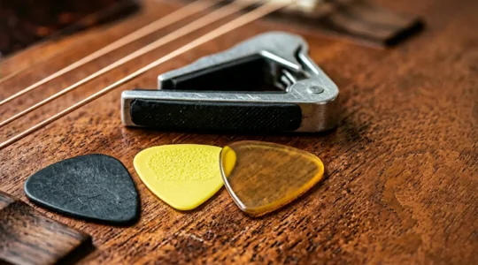 Close-up of guitar picks and capo on wooden surface with guitar strings