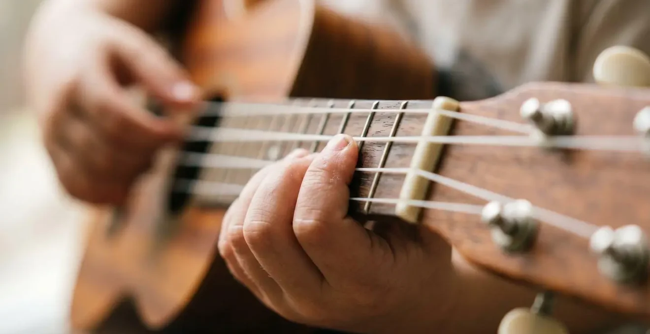 Close-up view of small child hands forming their first chord on a ukulele, showing finger placement and grip technique