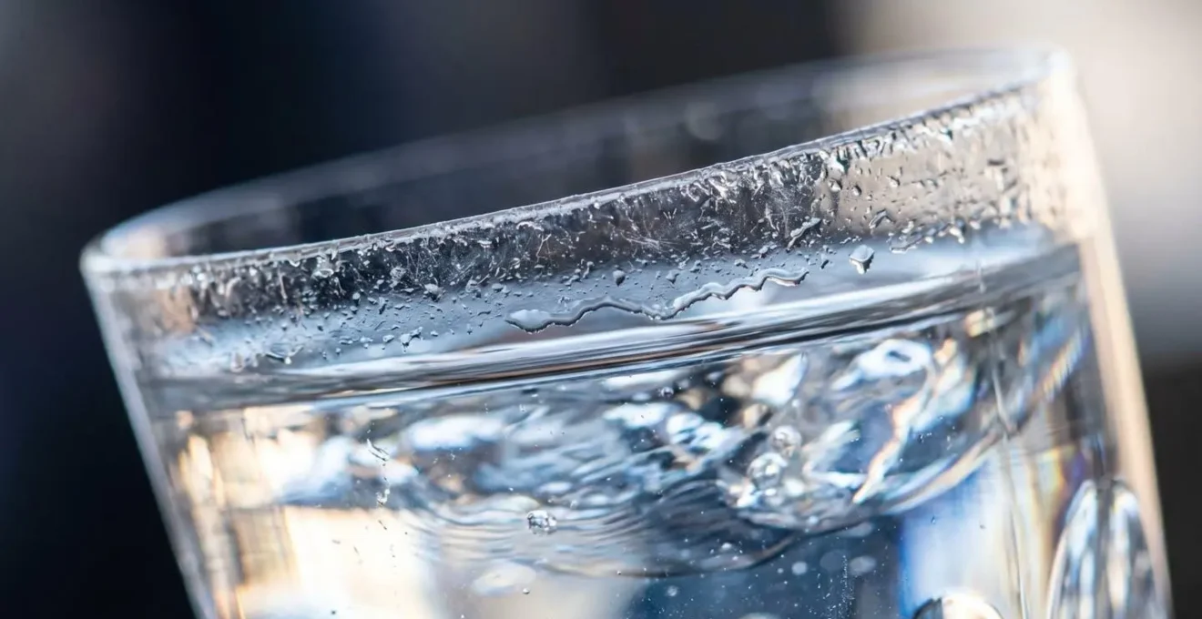 Extreme macro close-up of wine glass rim with water showing surface tension and light refraction for granular synthesis sound source